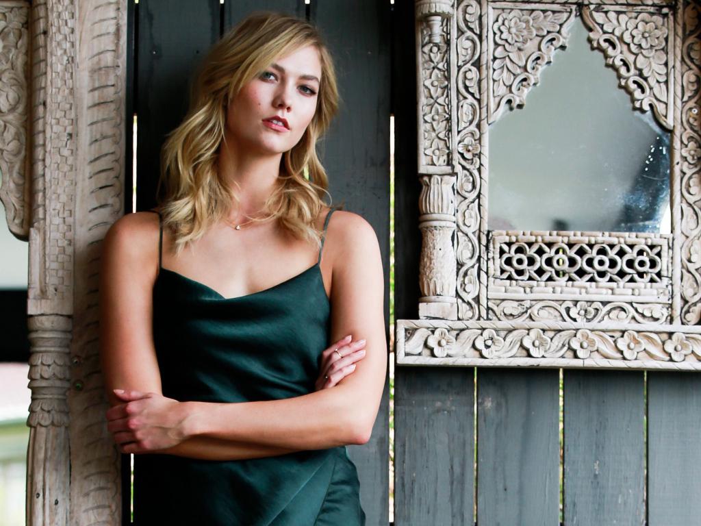 Красивая стильная модель Карли Клосс стоит у стены с зеркалом