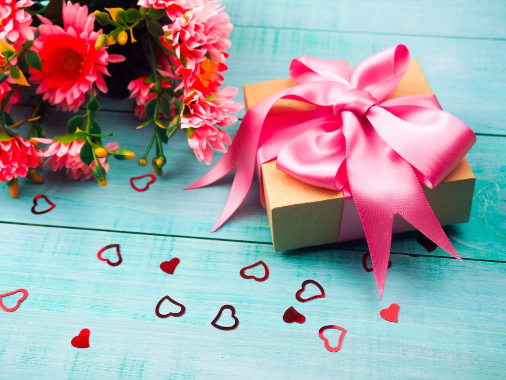 Подарок с розовым бантом на голубом столе с букетом