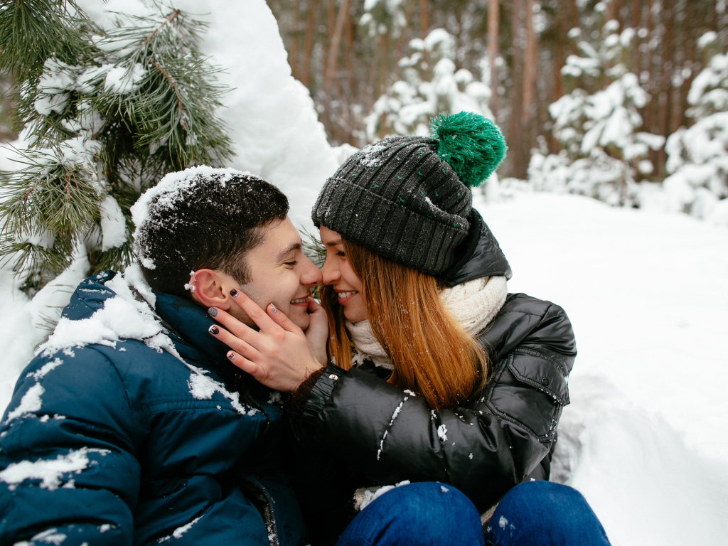 Влюбленная пара сидит под заснеженной еловой веткой зимой