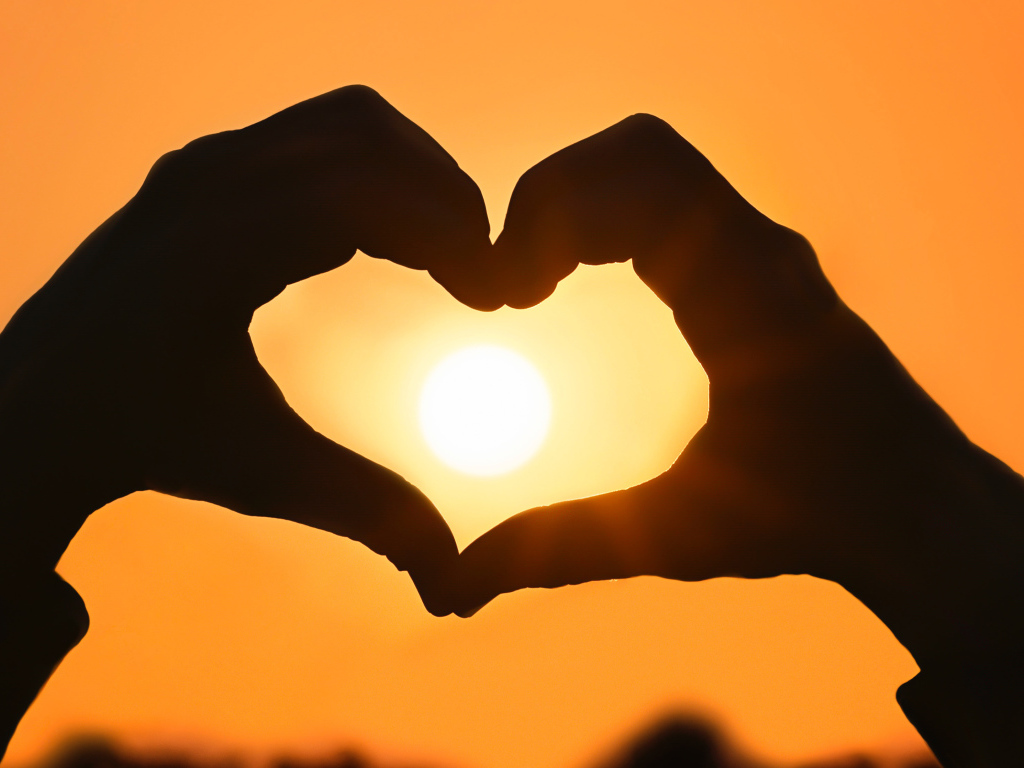 Сердце руками на фоне солнца в небе