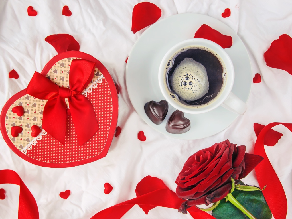 Кружка с кофе и шоколадными конфетами на столе с подарком и красной розой 