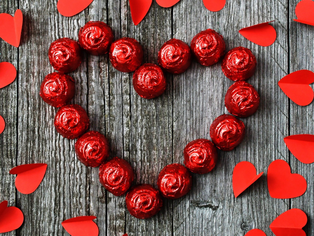 Красное сердце из конфет на деревянном фоне с бумажными сердечками