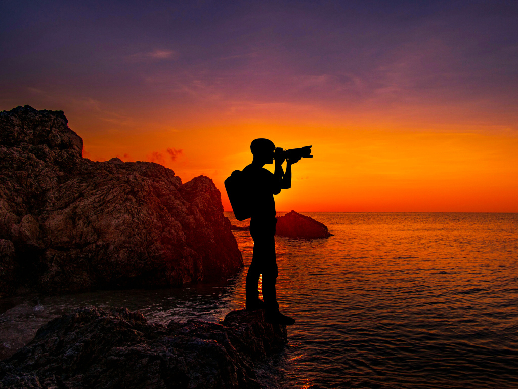 Мужчина фотографирует закат на берегу моря