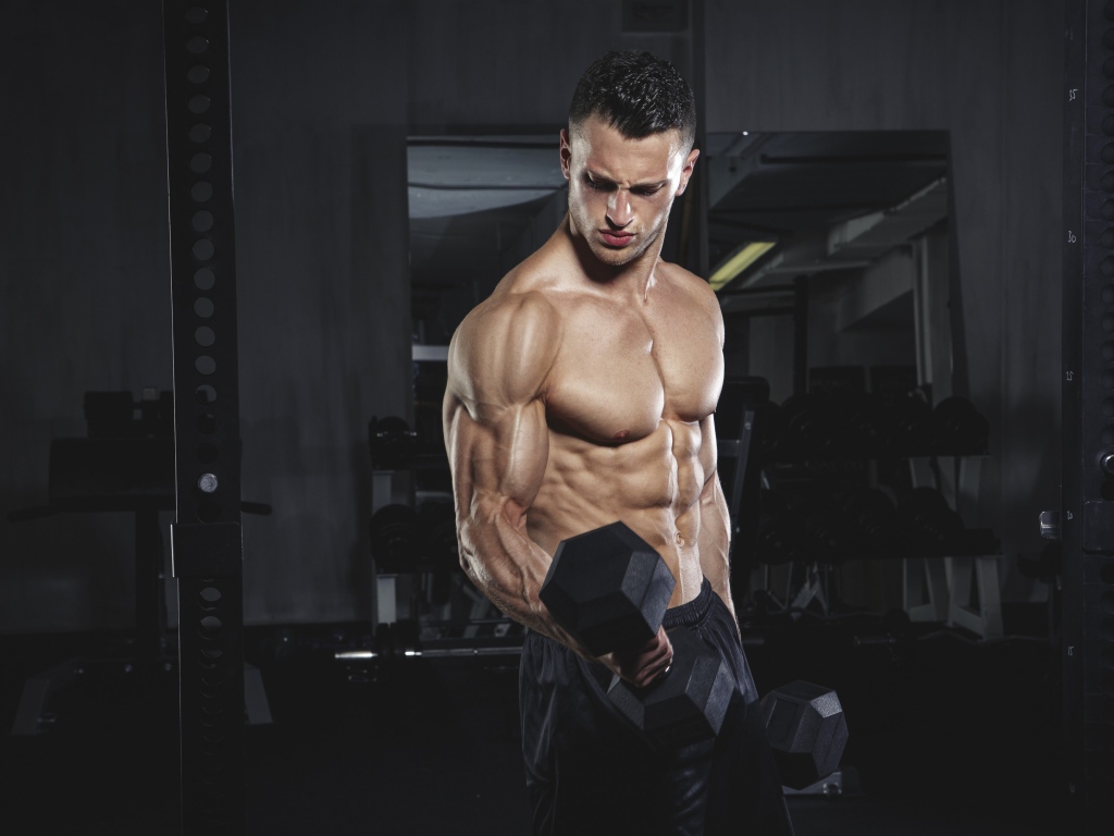 Накаченный мужчина с тяжелыми гантелями в руках 