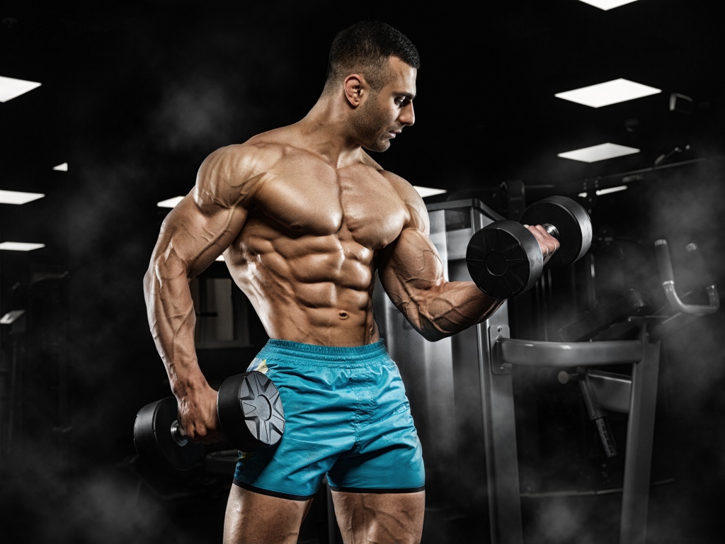 Сильный накаченный мужчина в шортах с гантелями в руках 