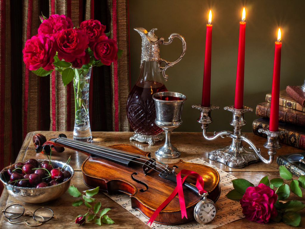 Зажженные красные свечи на столе букетом роз, скрипкой и черешней 