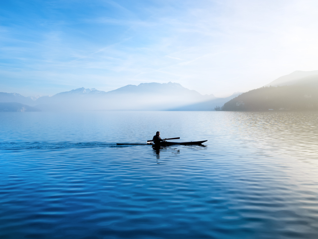 Мужчина плывет на лодке на фоне гор