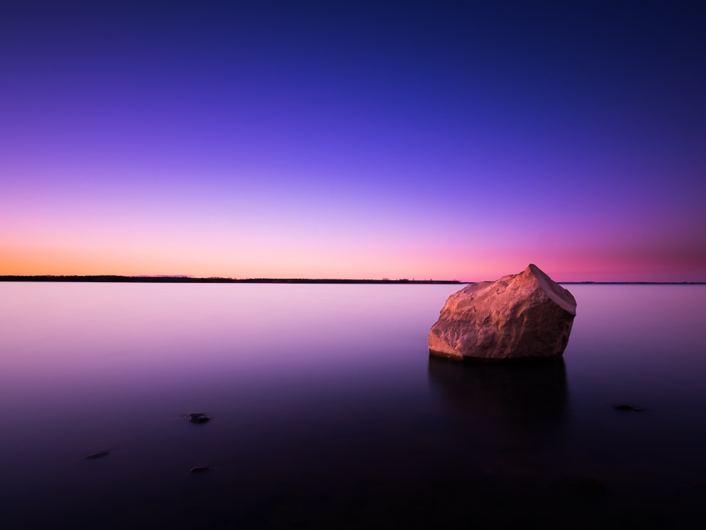 Большой камень в спокойной воде в сумерках