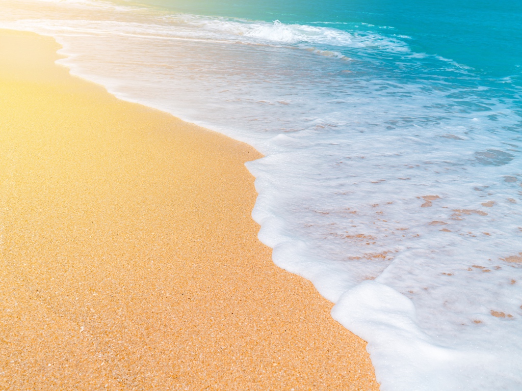 Белые волны океана омывают желтый горячий песок на пляже