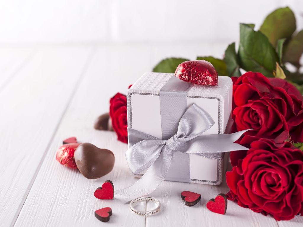 Подарок на столе с конфетами и букетом красных роз 