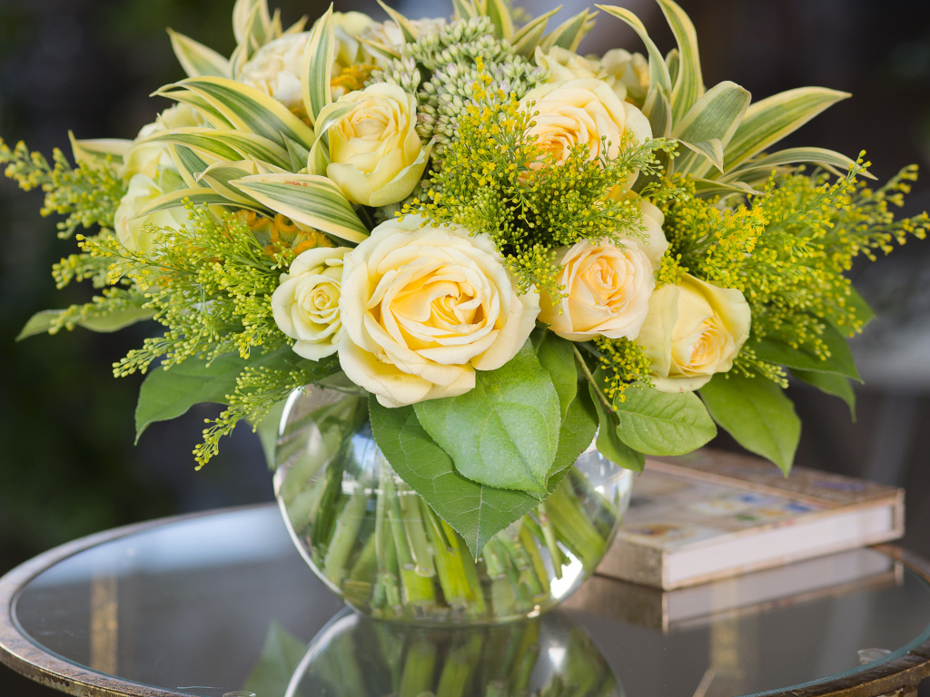 Красивый букет роз с зелеными листьями в в вазе на стеклянном столе