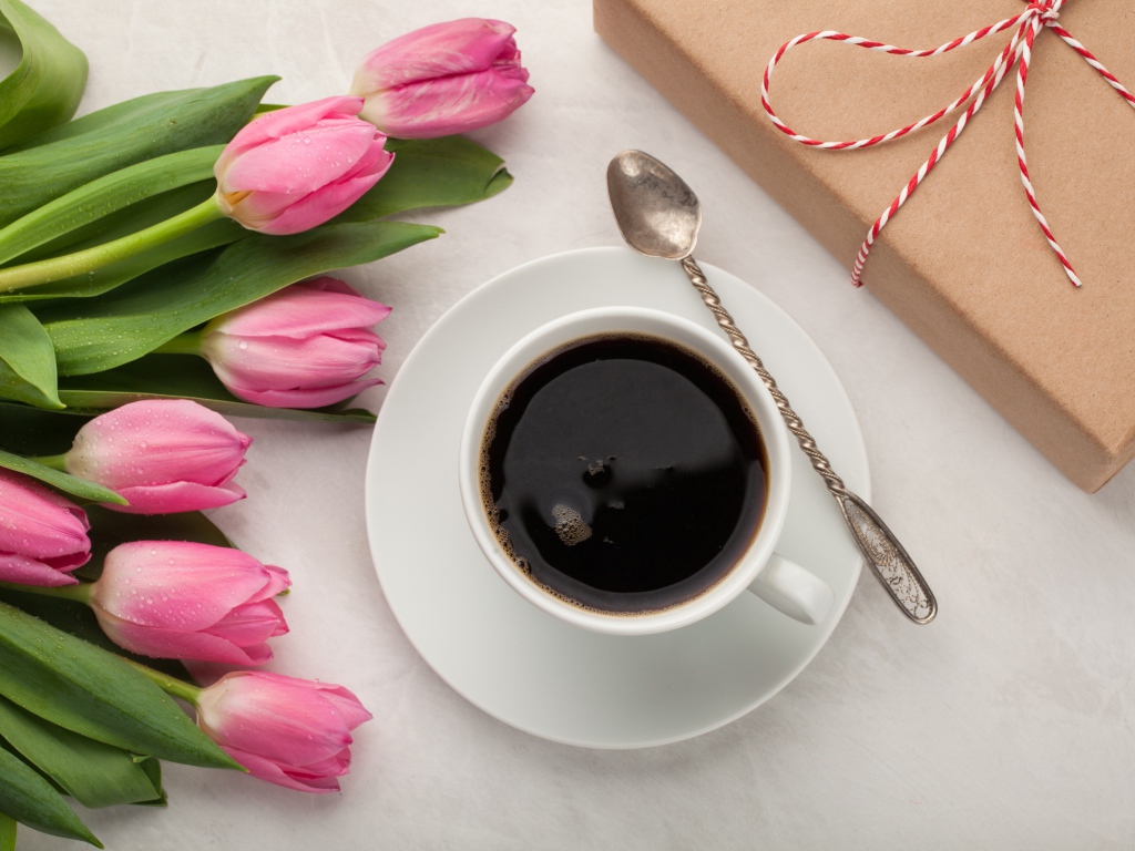 Белая чашка кофе на столе букетом розовых тюльпанов и подарком