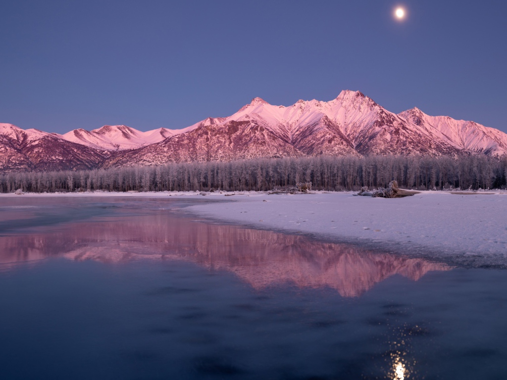 Луна над заснеженными горами отражается в заледеневшем озере 