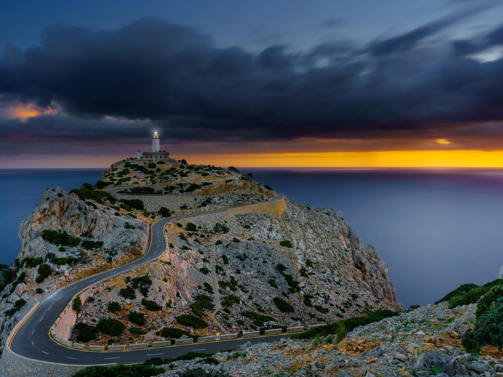 Извилистая дорога ведет к маяку на краю скалы под пасмурным небом