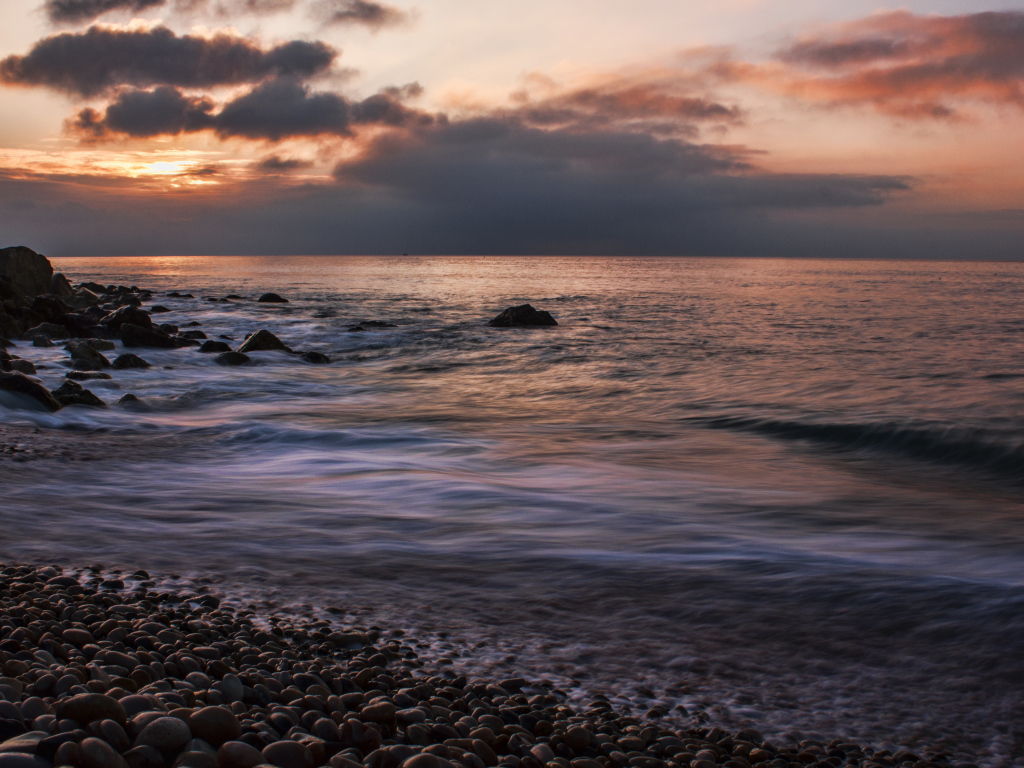 Мелкие камни на берегу моря на закате