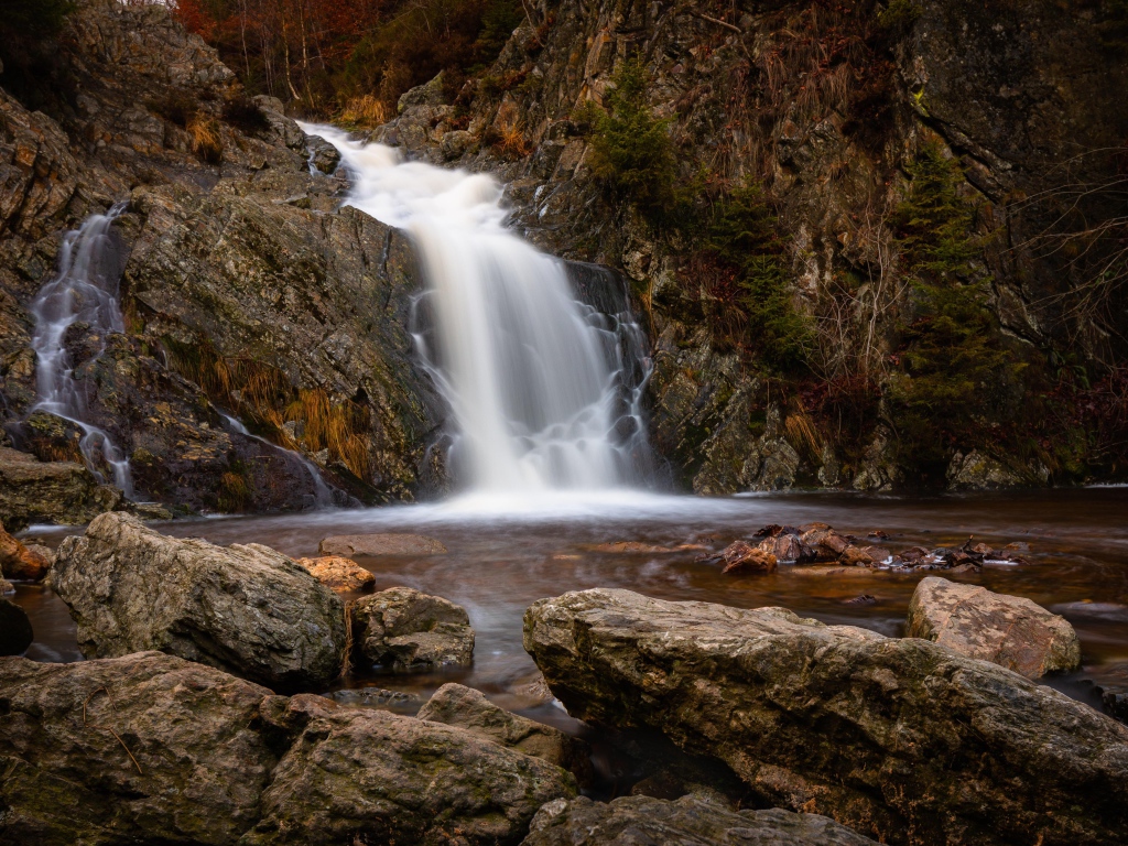 Быстрая вода водопада стекает по камням в горную реку