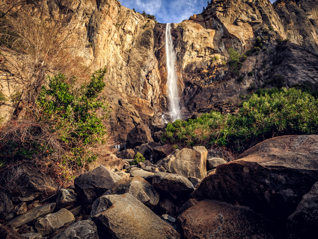 Водопад стекает с высокой скалы на камни 