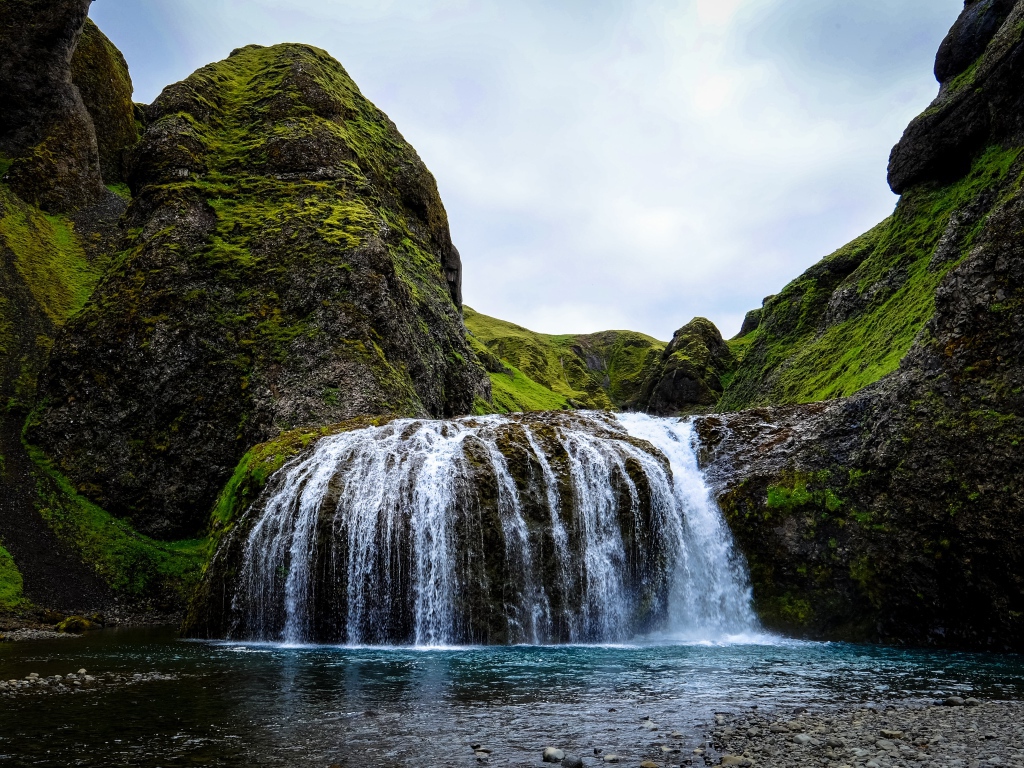 Белая вода водопада стекает по покрытым мхом скалам