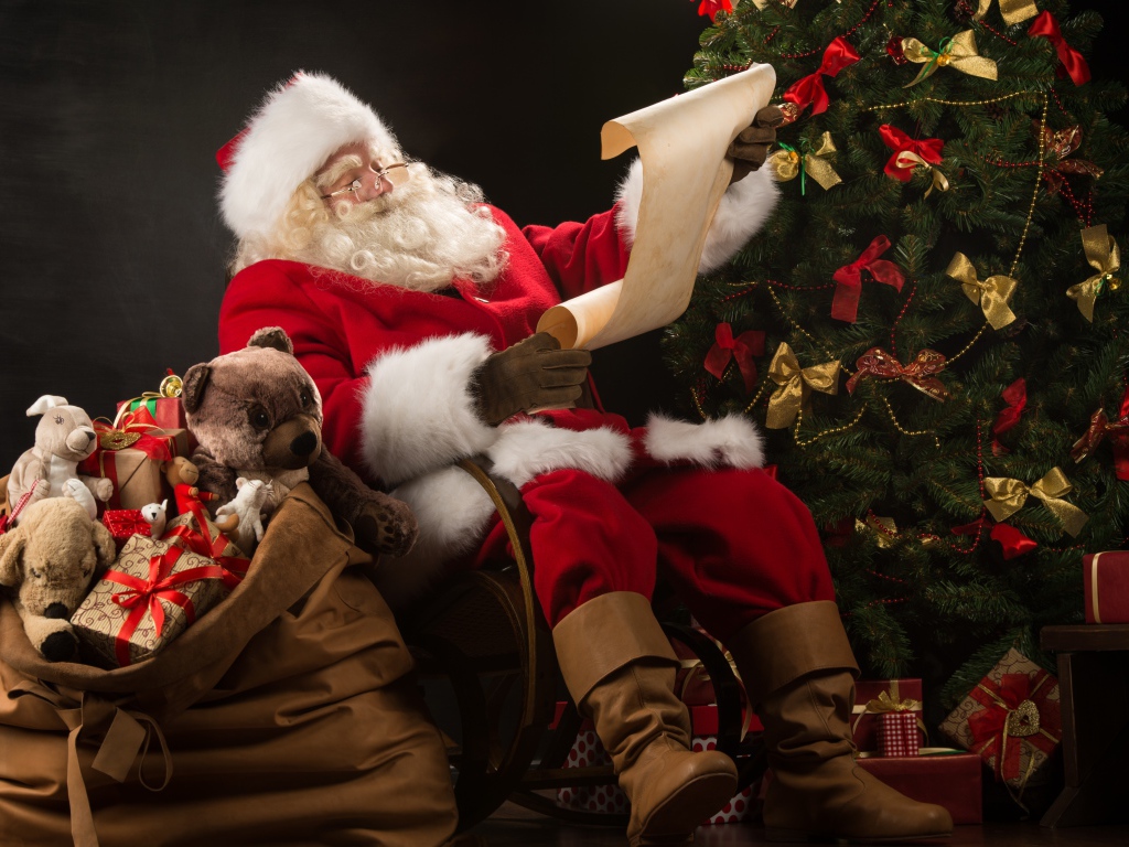Санта Клаус с мешком подарков читает у елки