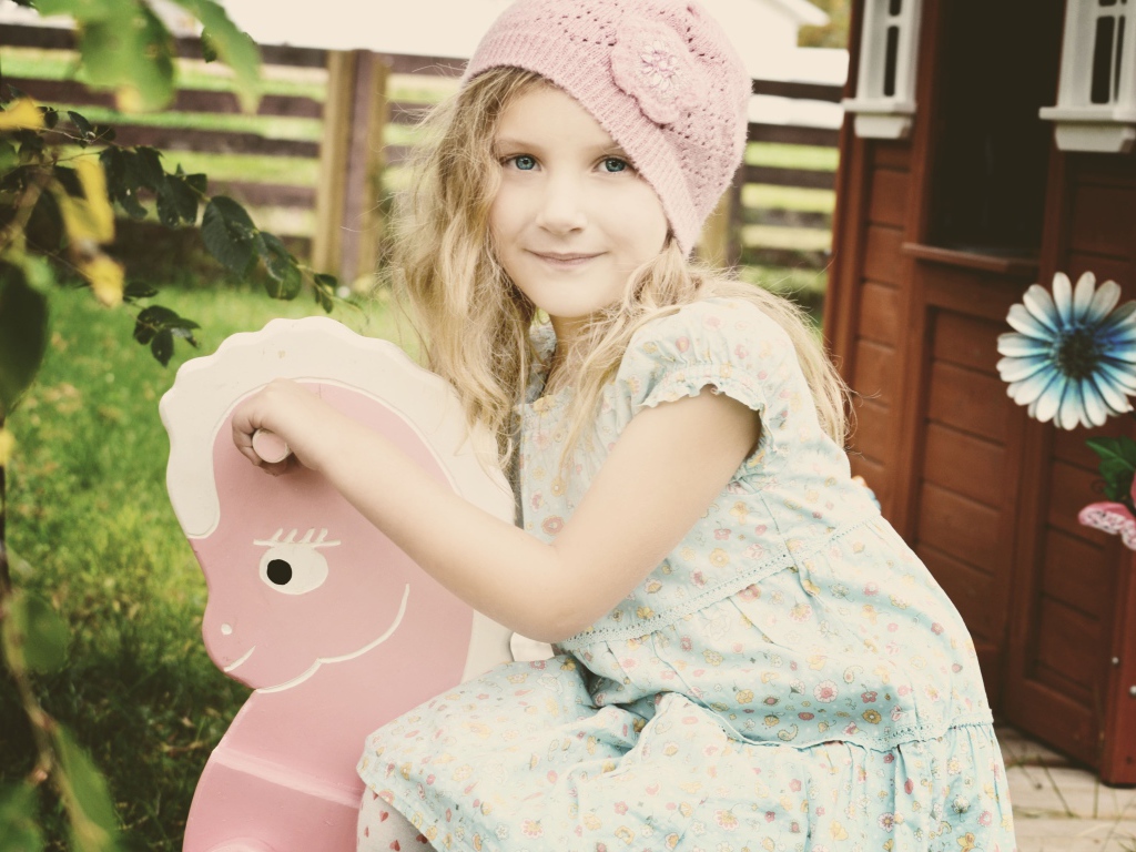 Девочка в платье сидит на деревянной лошади