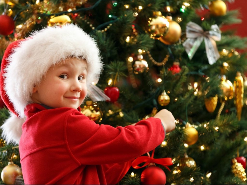 Мальчик в шапке Санта Клауса наряжает елку