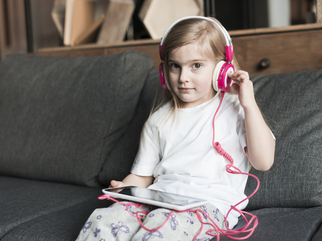 Девочка сидит на диване в наушниках  и с планшетом