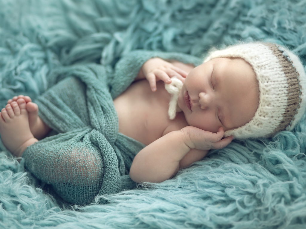 Маленький ребенок в вязаной шапке спит на меховом покрывале