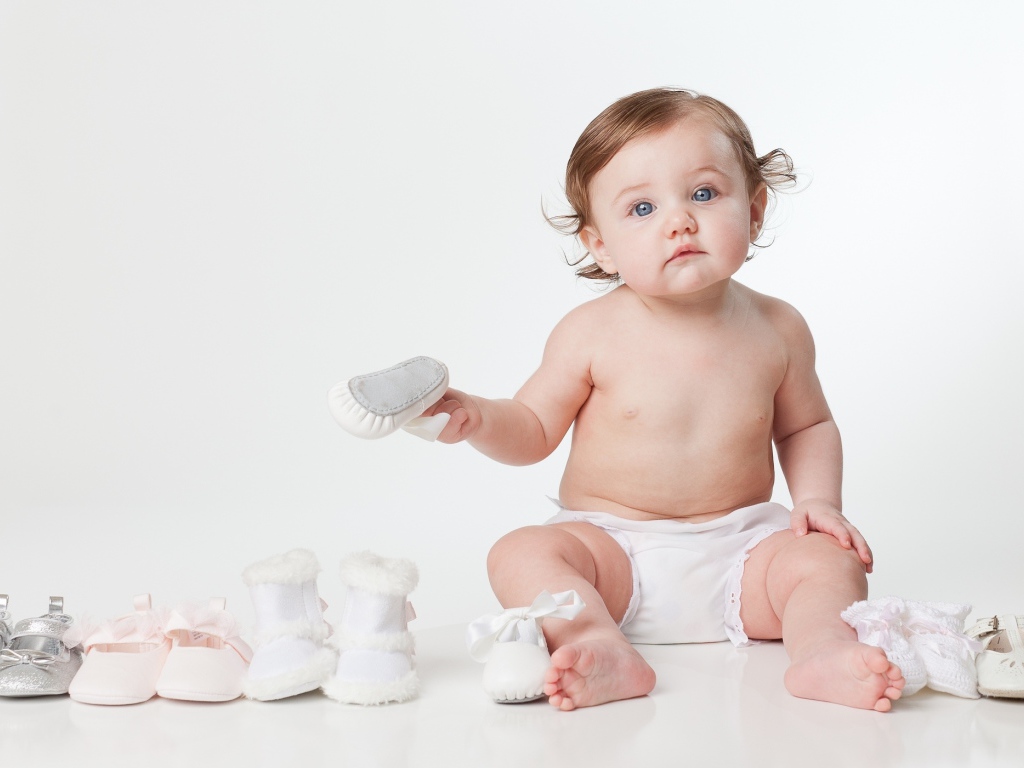 Маленький забавный голубоглазый малыш с обувью на белом фоне