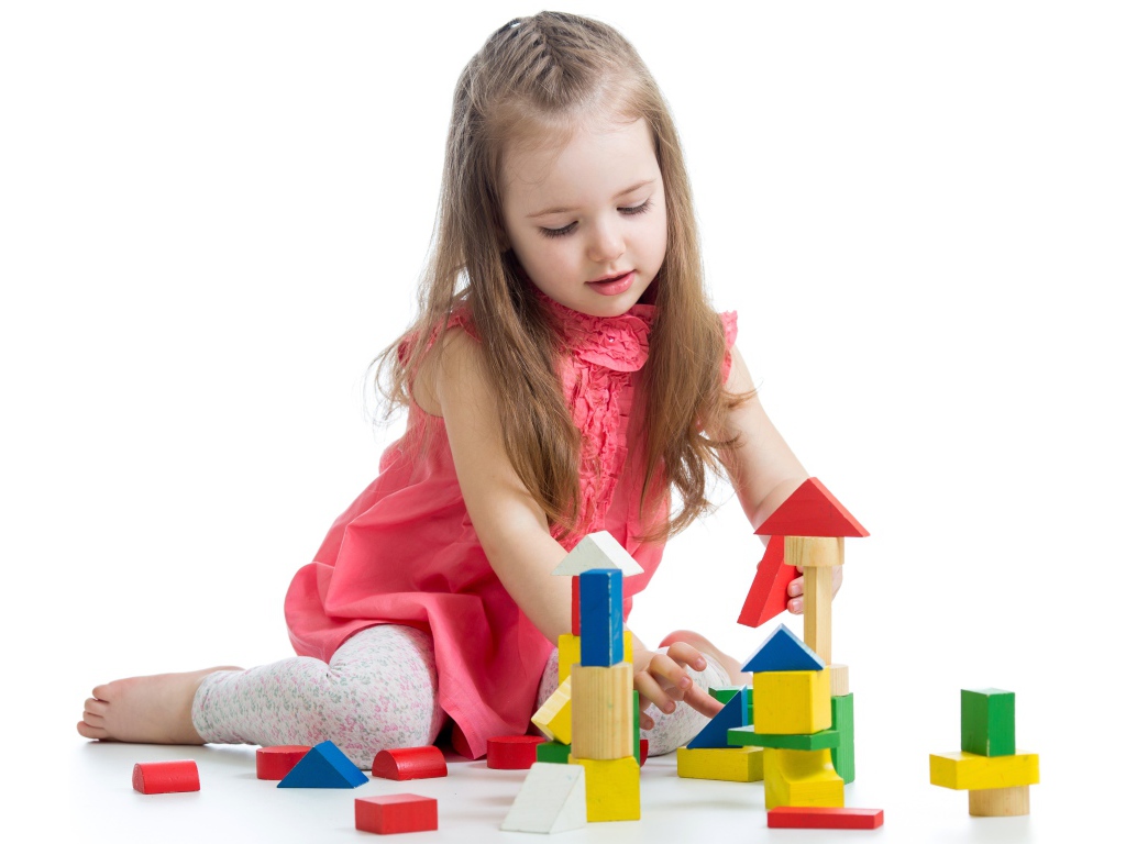 Маленькая девочка строит домик из кубиков на белом фоне