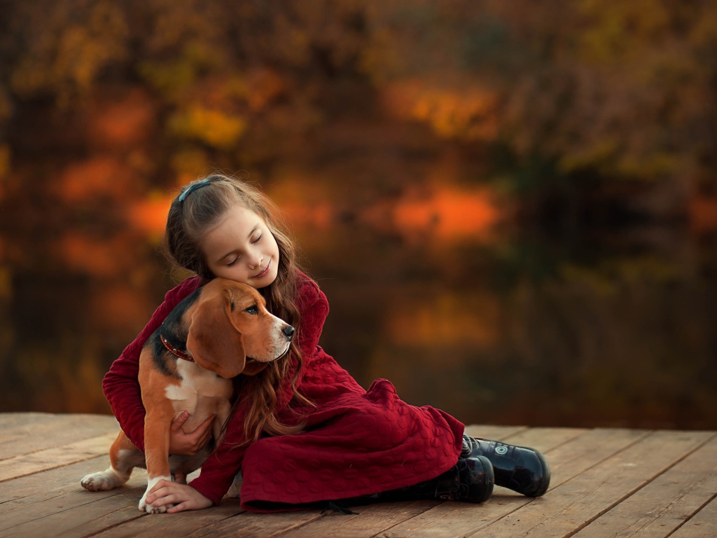 Маленькая девочка обнимает собаку породы бигль на мосту