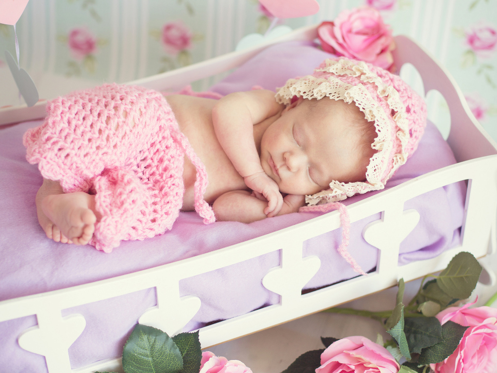 Спящий ребенок в розовом вязаном костюме в колыбели
