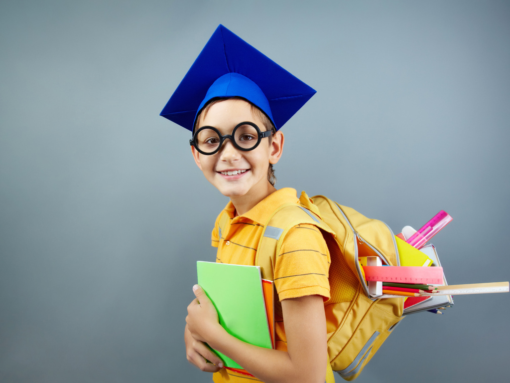 Умный школьник в очках со школьными принадлежностями на сером фоне