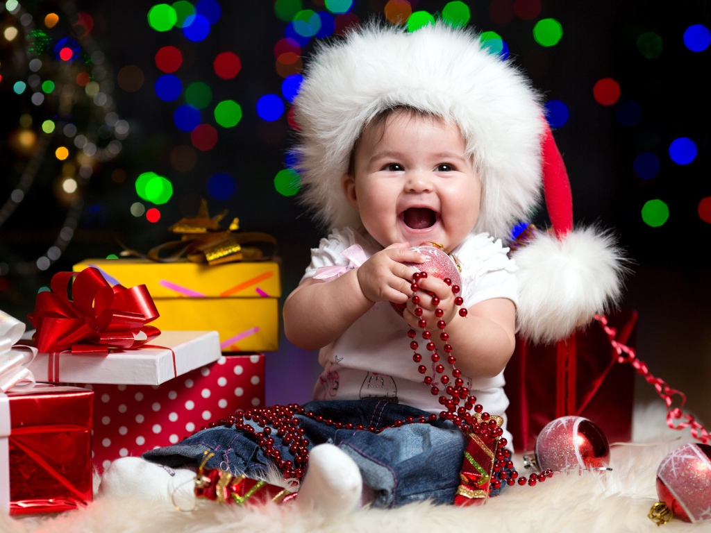 Улыбающийся малыш в новогодней шапке с подарками у елки