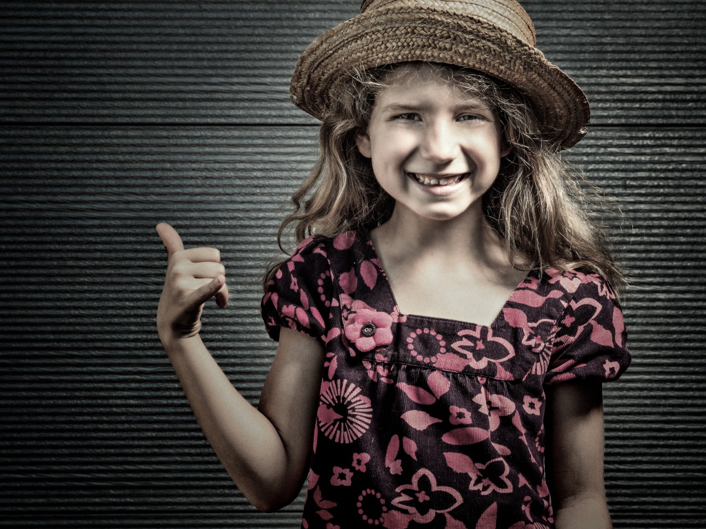 Улыбающаяся девочка в соломенной шляпе у стены 