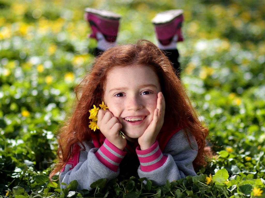 Улыбающаяся рыжеволосая девочка лежит на зеленой траве