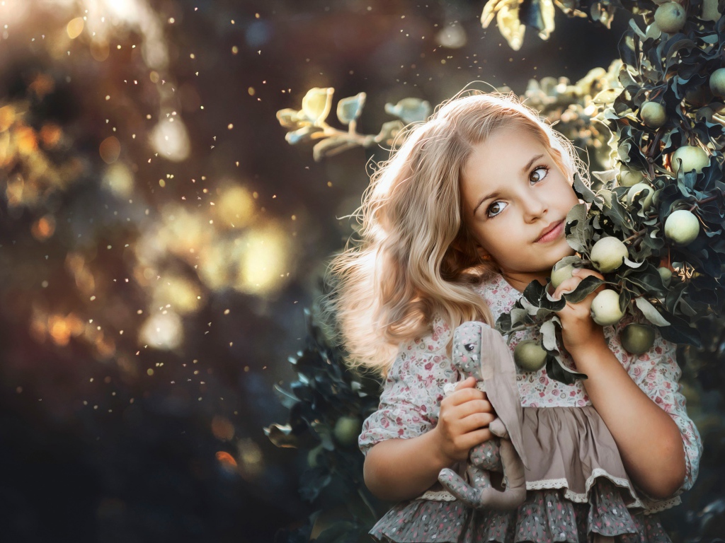 Маленькая девочка стоит у ветки с яблоками
