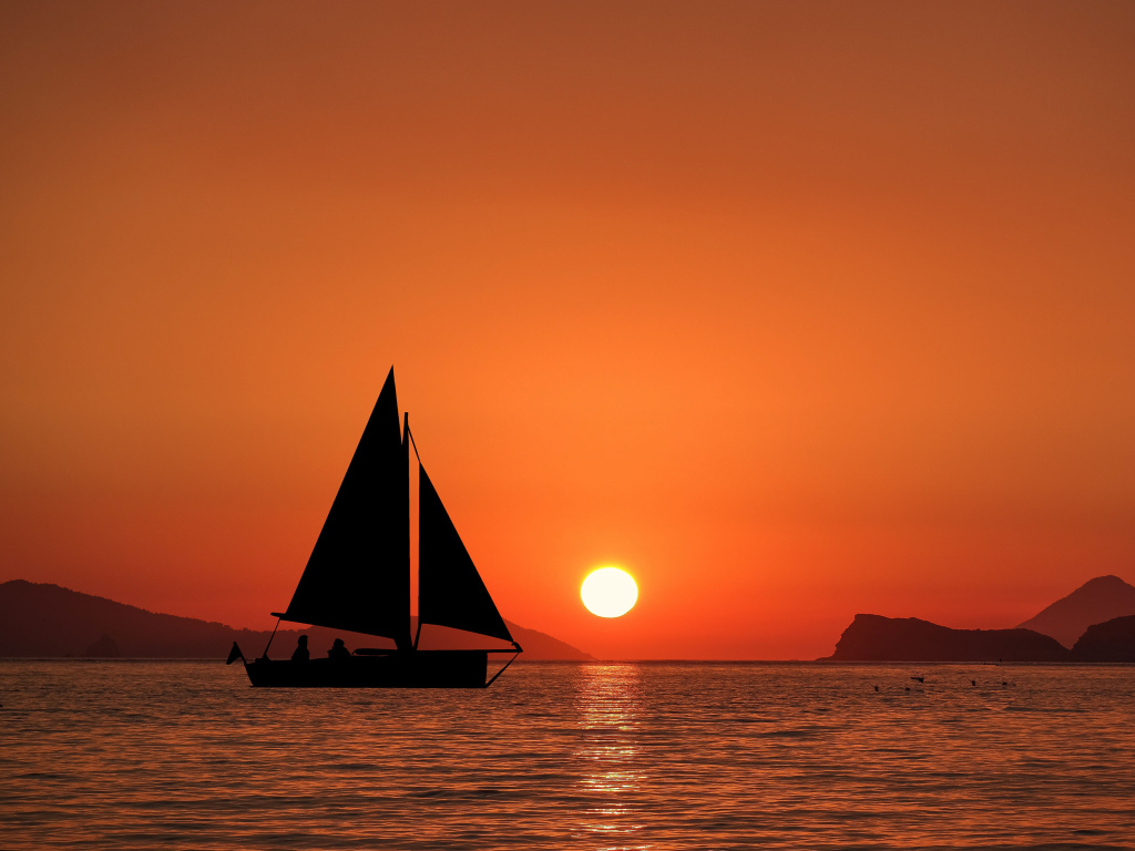 Парусная лодка в море на закате солнца