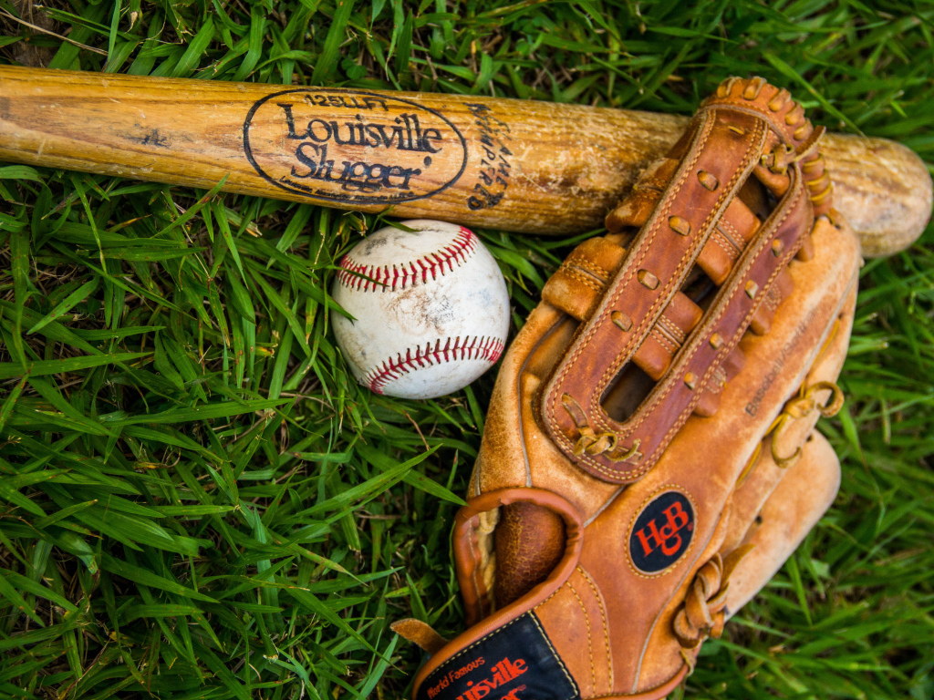 Бейсбольная бита, перчатка и мяч лежат на зеленой траве