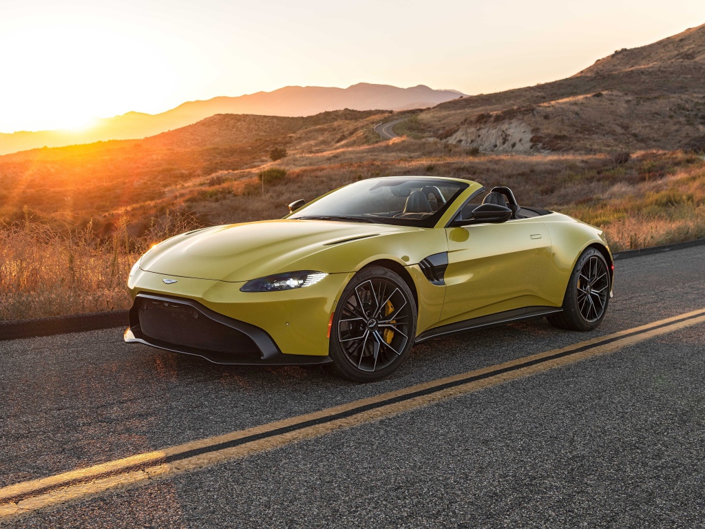 Желтый кабриолет  Aston Martin Vantage Roadster, 2021 года на трассе на рассвете