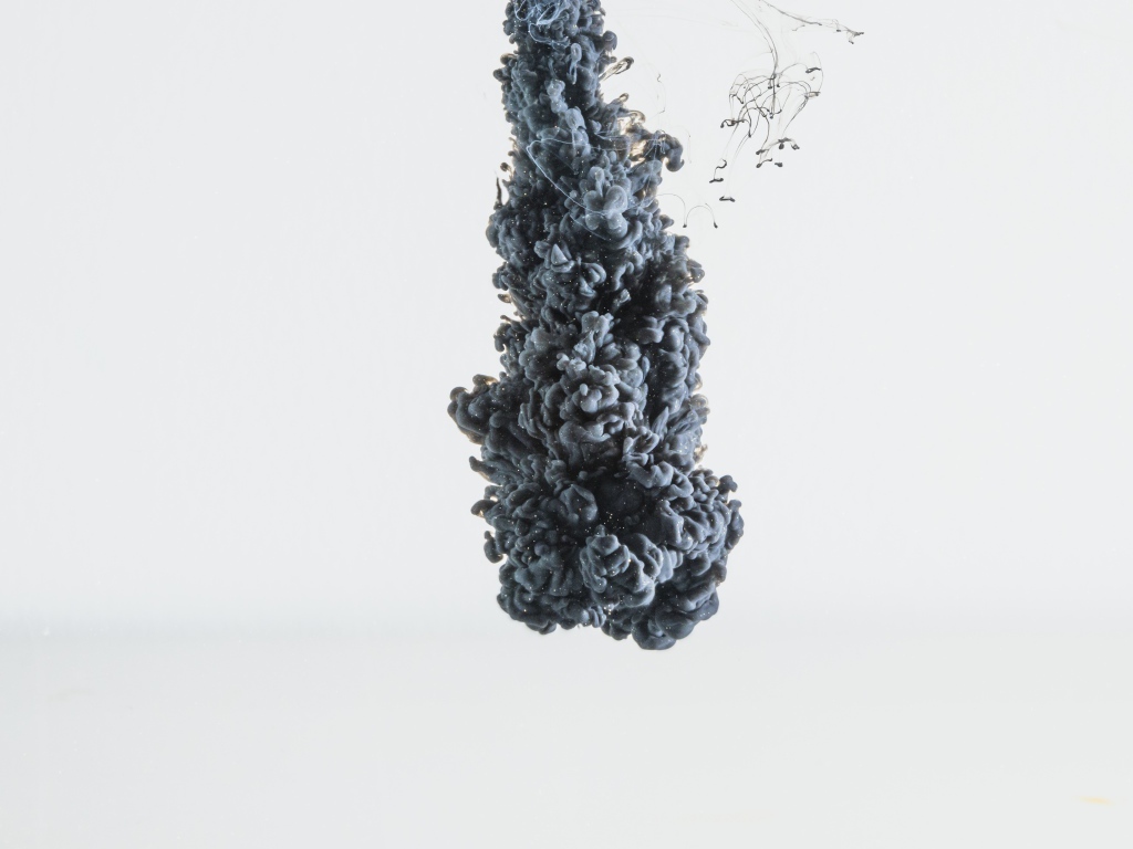 Черная краска растворяется в воде на белом фоне 