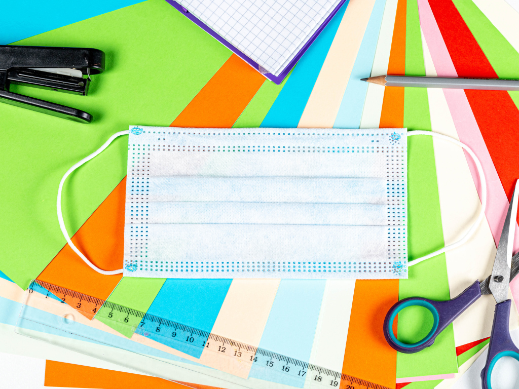 Маска от коронавируса лежит на цветной бумаге с канцелярскими предметами