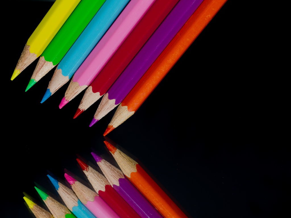 Multi-colored pencils are reflected in a black mirror surface