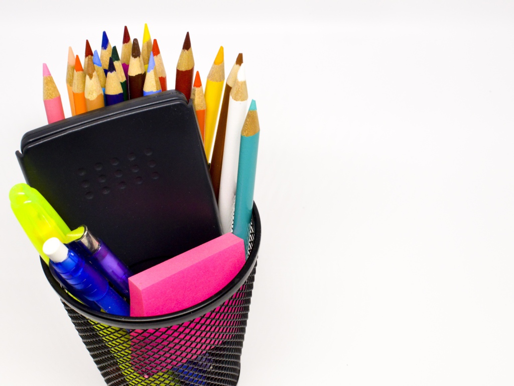 Канцелярские предметы в черном стакане на белом фоне 