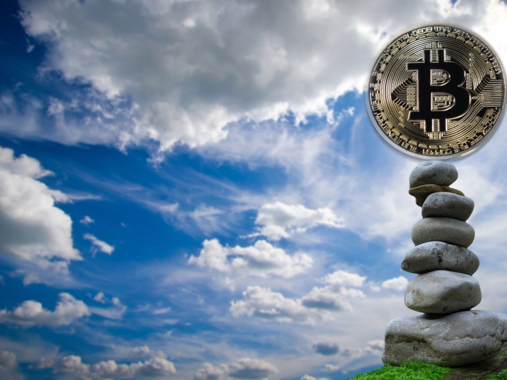 Монета биткоин стоит на камнях на фоне неба