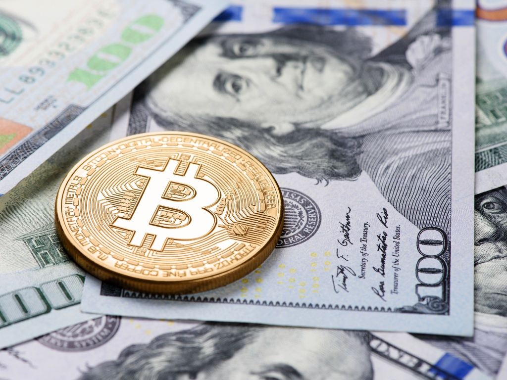 Золотая монета биткоин лежит на долларах 