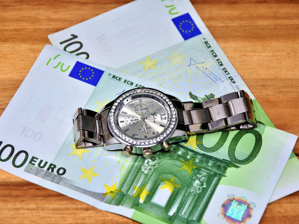 Две купюры по сто евро с часами на столе 