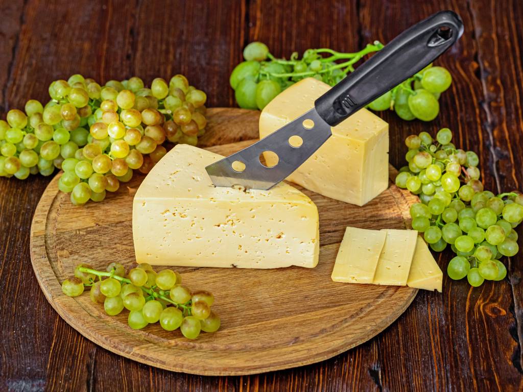 A piece of hard cheese on a table with a knife and white grapes