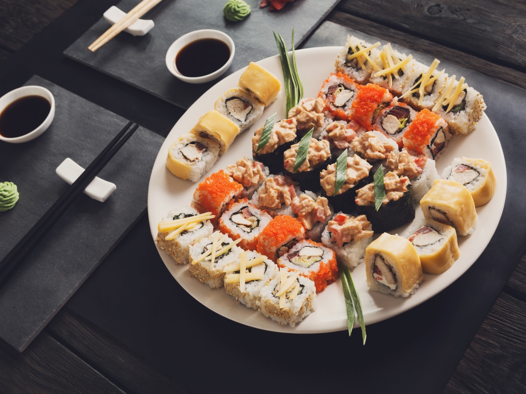 Аппетитные роллы на большой тарелке на столе с соусом