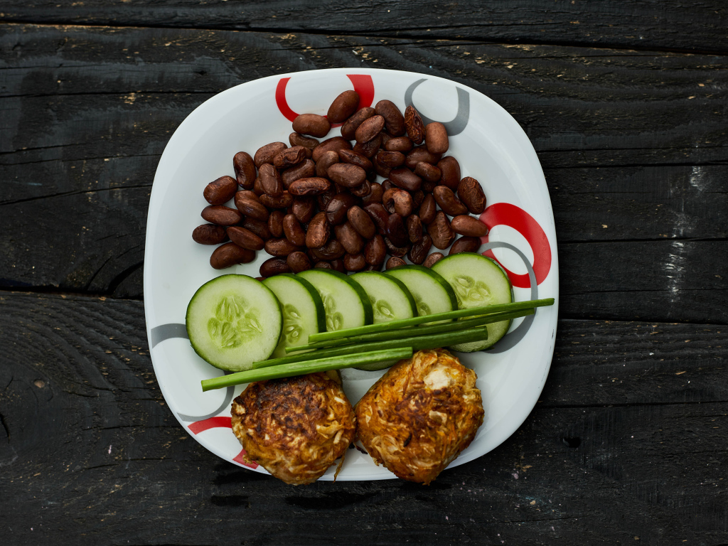 Фасоль на тарелке с оладьями и огурцами 