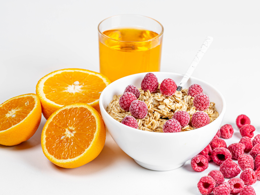 Миска мюсли с ягодами малины и апельсинами на столе с соком